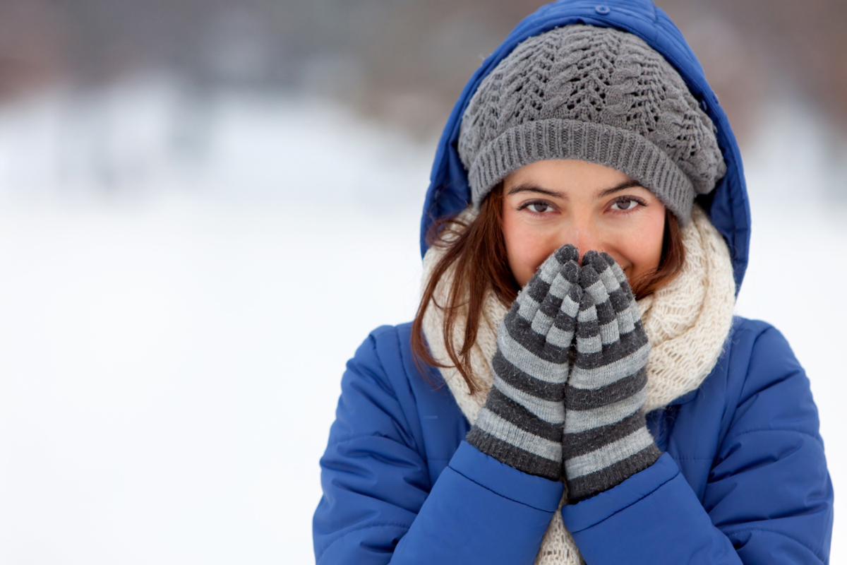 Een glimlachende vrouw, ingepakt in een sjaal en muts in de winter, genietend van de voordelen van essentiële oliën om haar immuniteit te verhogen en haar te beschermen tegen de kou.