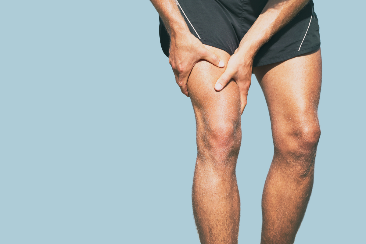 A person suffering from a cramp in the thigh, holding the leg after physical effort.