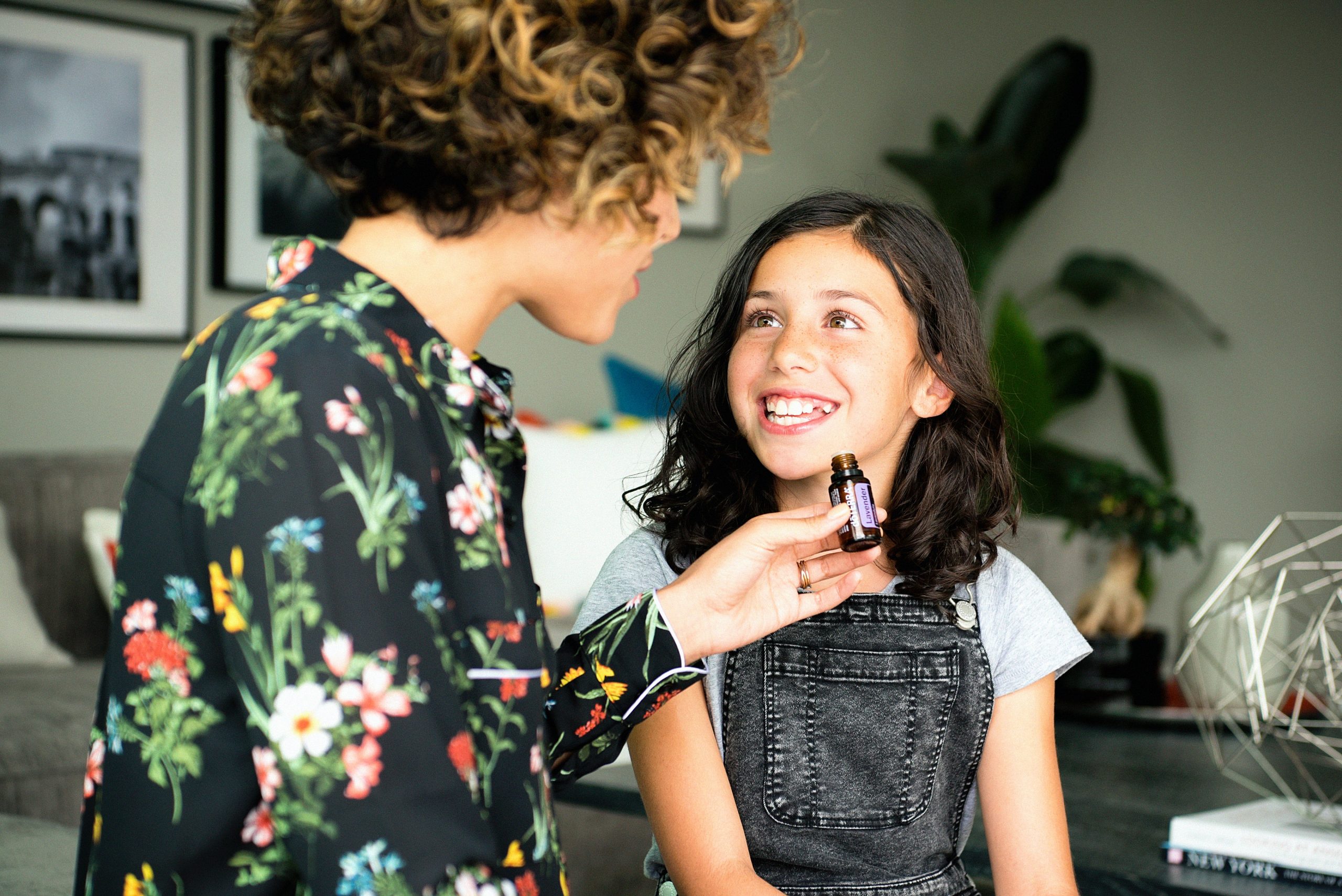 Une mère tenant un flacon d’huile essentielle de lavande devant sa fille souriante, illustrant l’utilisation sécurisée des huiles essentielles pour les enfants.