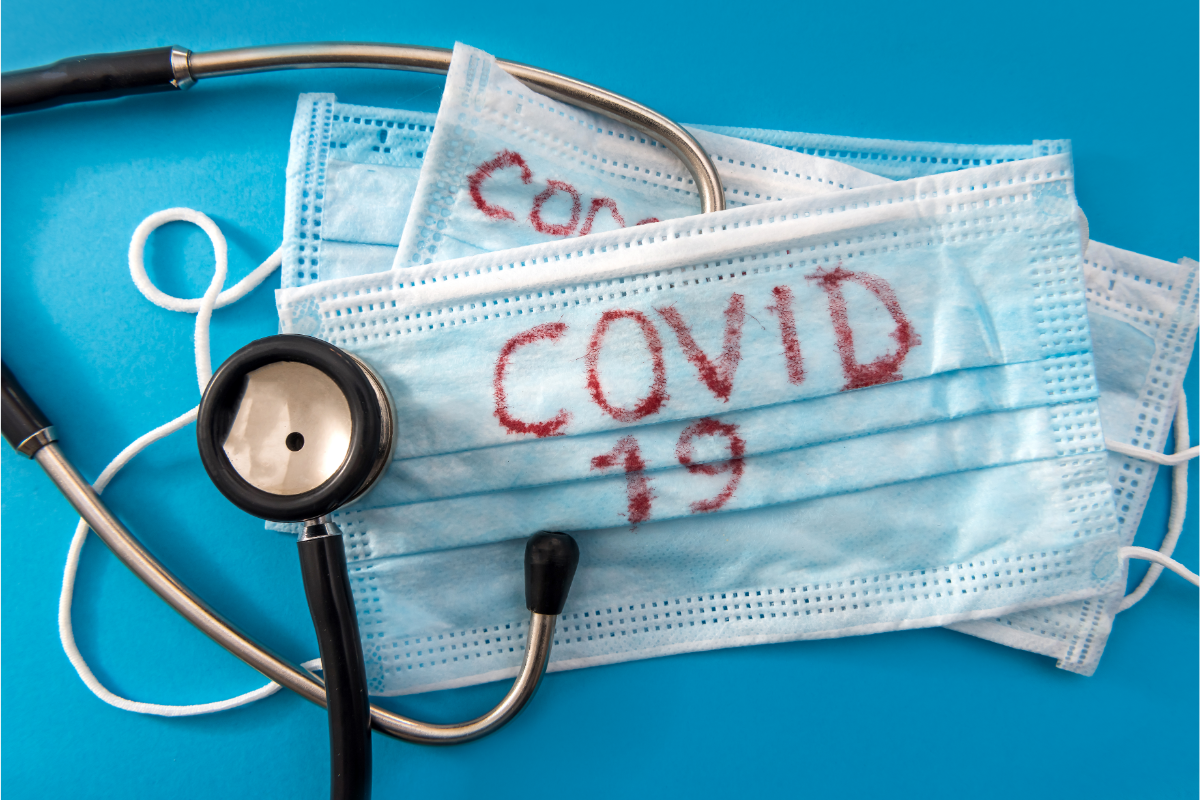 Un stéthoscope et des masques chirurgicaux superposés, sur fond bleu, avec "COVID-19" écrit en rouge sur les masques, symbolisent les efforts médicaux et les mesures de protection contre le coronavirus en 202