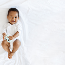 Bébé souriant tenant un anneau de dentition, symbole de bien-être et de douceur, en lien avec l’homéopathie pour les troubles du nourrisson.