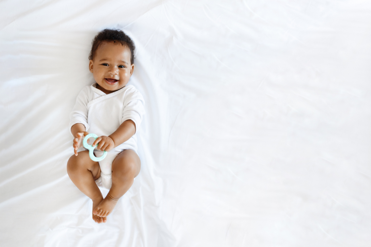 Een lachende baby die een bijtring vasthoudt, een symbool van welzijn en zachtheid, in verband met homeopathie voor kinderziektes.