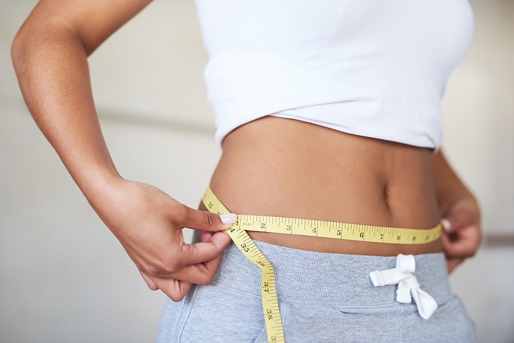 L'image représente une femme en train de se mesurer le tour de taille avec un mètre ruban. Zoom sur le protocole de diète protéinée médicale