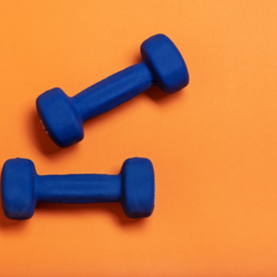 Haltères bleus sur fond orange, symbolisant l’activité physique et le renforcement musculaire dans un programme de perte de poids.