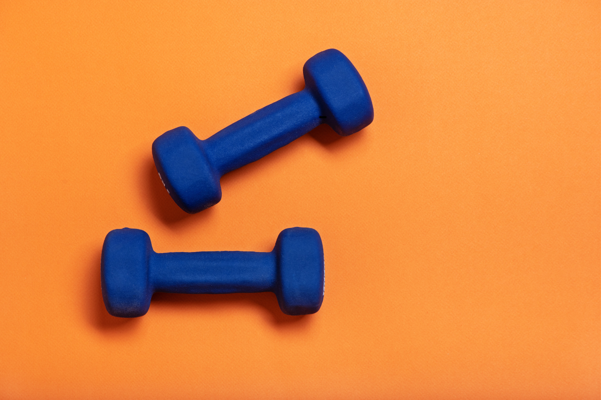 Mancuernas azules sobre fondo naranja, símbolo de la actividad física y el fortalecimiento muscular como parte de un programa de pérdida de peso.