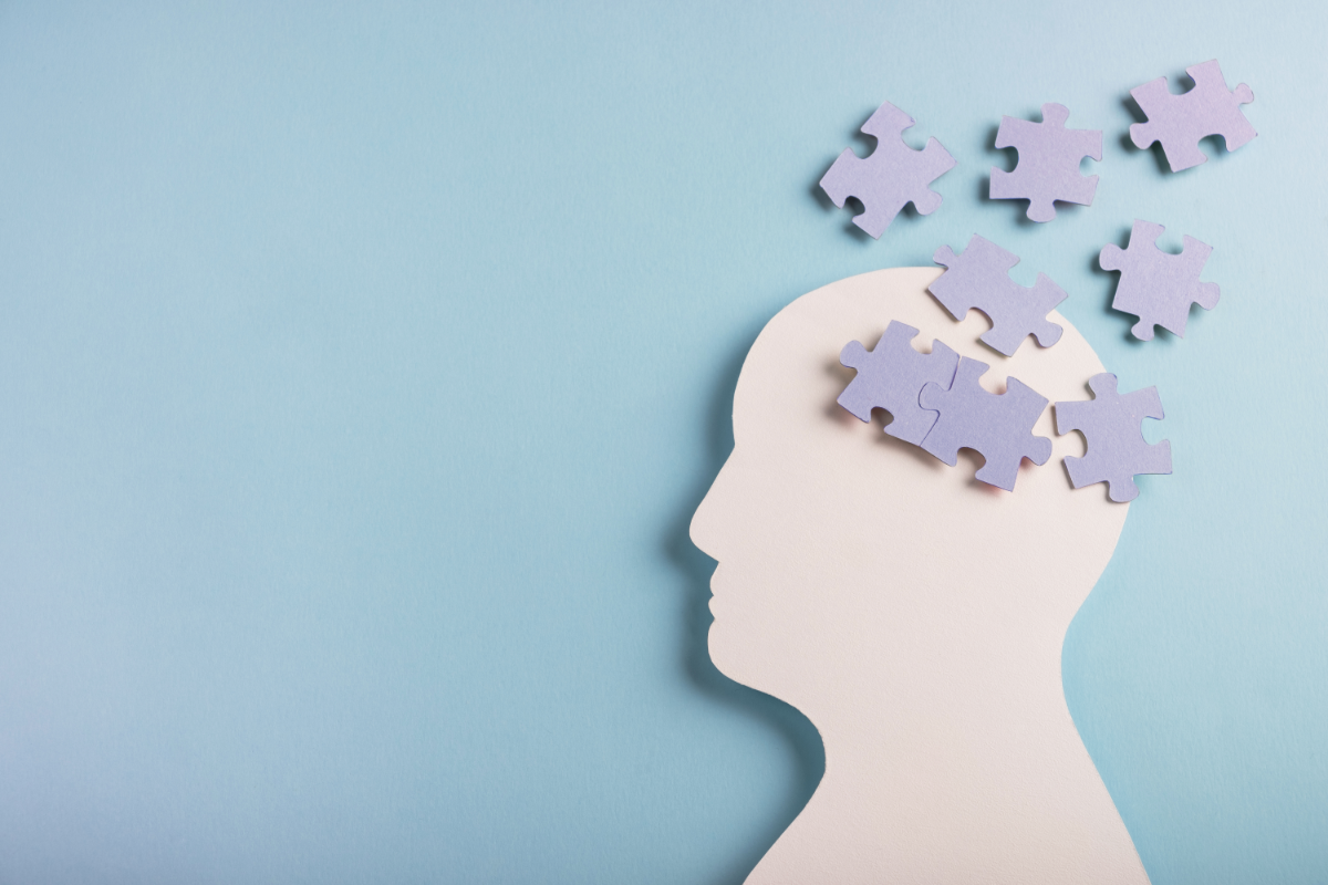 Image d'une silhouette de tête humaine en papier découpée sur un fond bleu pastel, avec des pièces de puzzle en papier de différentes teintes de violet placées à l'emplacement du cerveau, certaines pièces flottant au-dessus de la tête, suggérant un assemblage incomplet. Cette illustration métaphorique peut représenter les effets de l'anxiété sur la fonction cognitive et les troubles de la mémoire, en évoquant l'idée de pièces manquantes dans le processus de mémorisation.