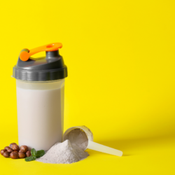 High-protein meal replacement shaker with powder and hazelnuts on yellow background