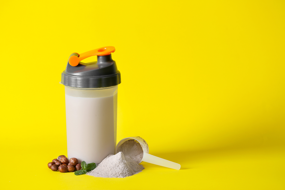 High-protein meal replacement shaker with powder and hazelnuts on yellow background