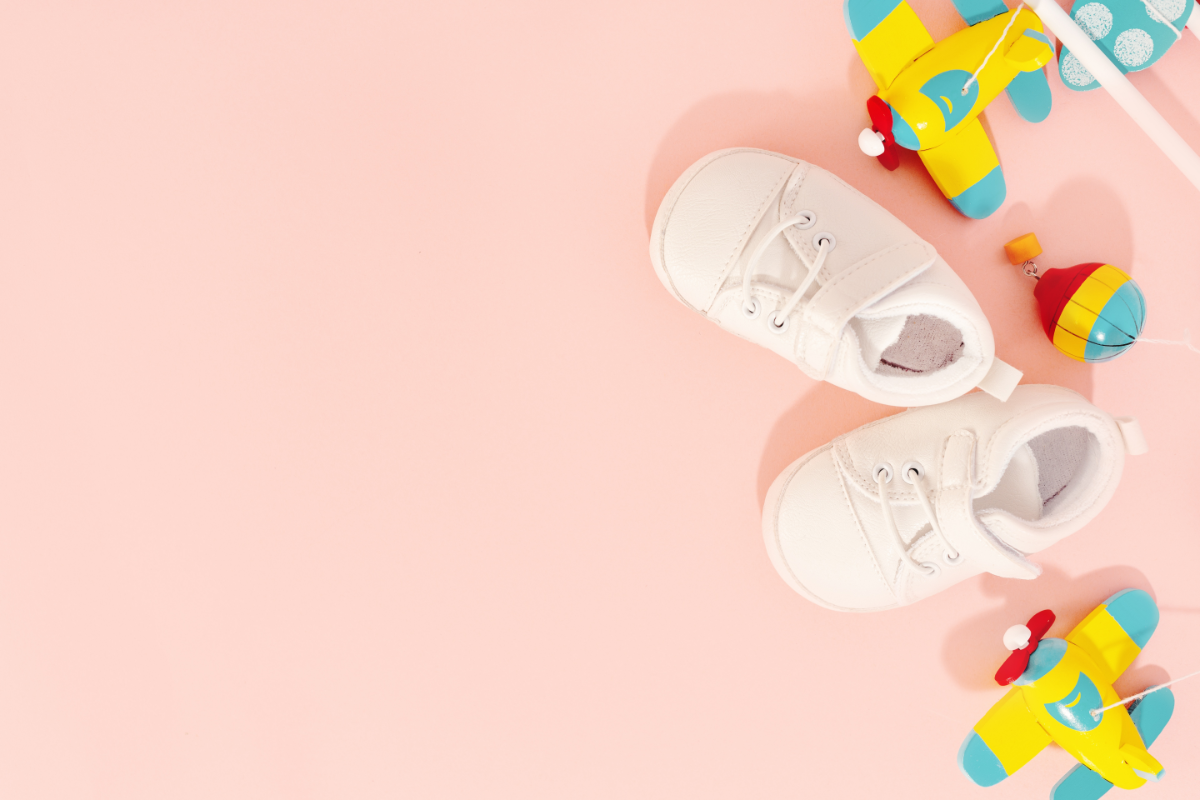 Que mettre dans sa trousse homéopathique pour la maternité. L'image représente des chaussures de bébé ainsi que des jouets, sur un fond rose.