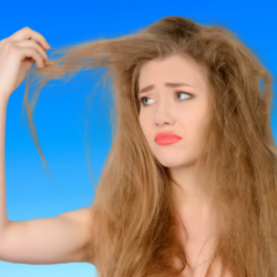 Una mujer con el cabello seco y dañado tira de un mechón, ilustrando los efectos de la sequedad capilar y la necesidad de cuidados nutritivos a base de aceites vegetales.