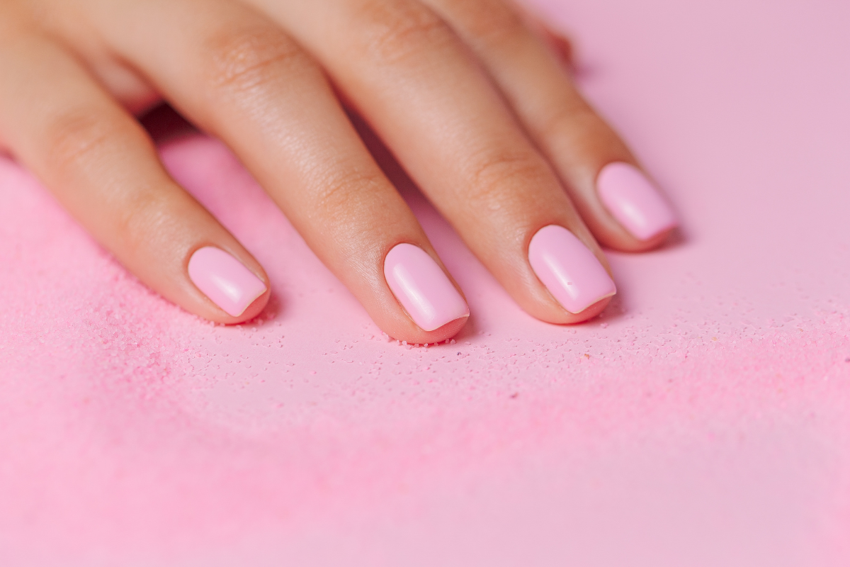 Feminine hand with pale pink varnish on pink background, symbolizing healthy, well-groomed nails.