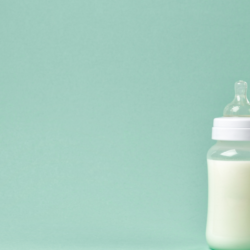 Un biberon rempli de lait avec une tétine ronde en silicone posé sur un fond uni de couleur vert pastel, évoquant la douceur et la simplicité de l'alimentation infantile.