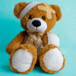 Ours en peluche marron avec un bandage sur la tête et des pansements adhésifs sur le corps posé contre un fond bleu uni.