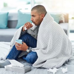 affections hivernales. Un homme sur son canapé, recouvert d'une couverture, avec un mouchoir dans les mains
