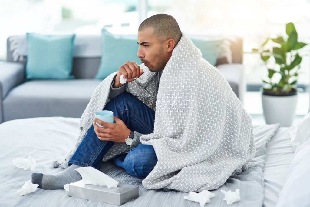 affections hivernales. Un homme sur son canapé, recouvert d'une couverture, avec un mouchoir dans les mains