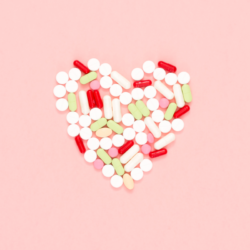 Un assemblage de pilules et de capsules pharmaceutiques formant un cœur sur un fond rose pâle, symbolisant l'importance des vitamines et des compléments alimentaires multivitamines pour la santé du cœur et le bien-être général.