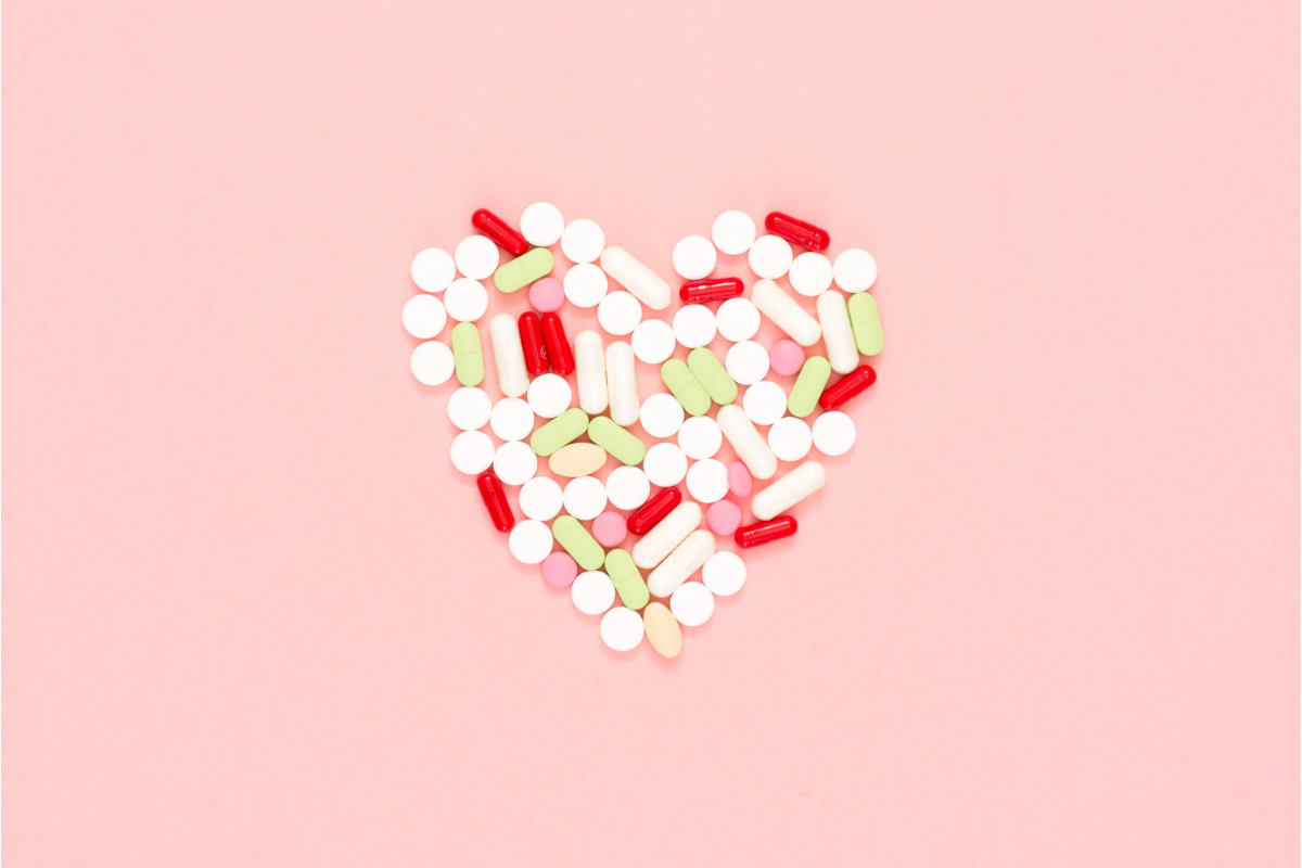 Un assemblage de pilules et de capsules pharmaceutiques formant un cœur sur un fond rose pâle, symbolisant l'importance des vitamines et des compléments alimentaires multivitamines pour la santé du cœur et le bien-être général.