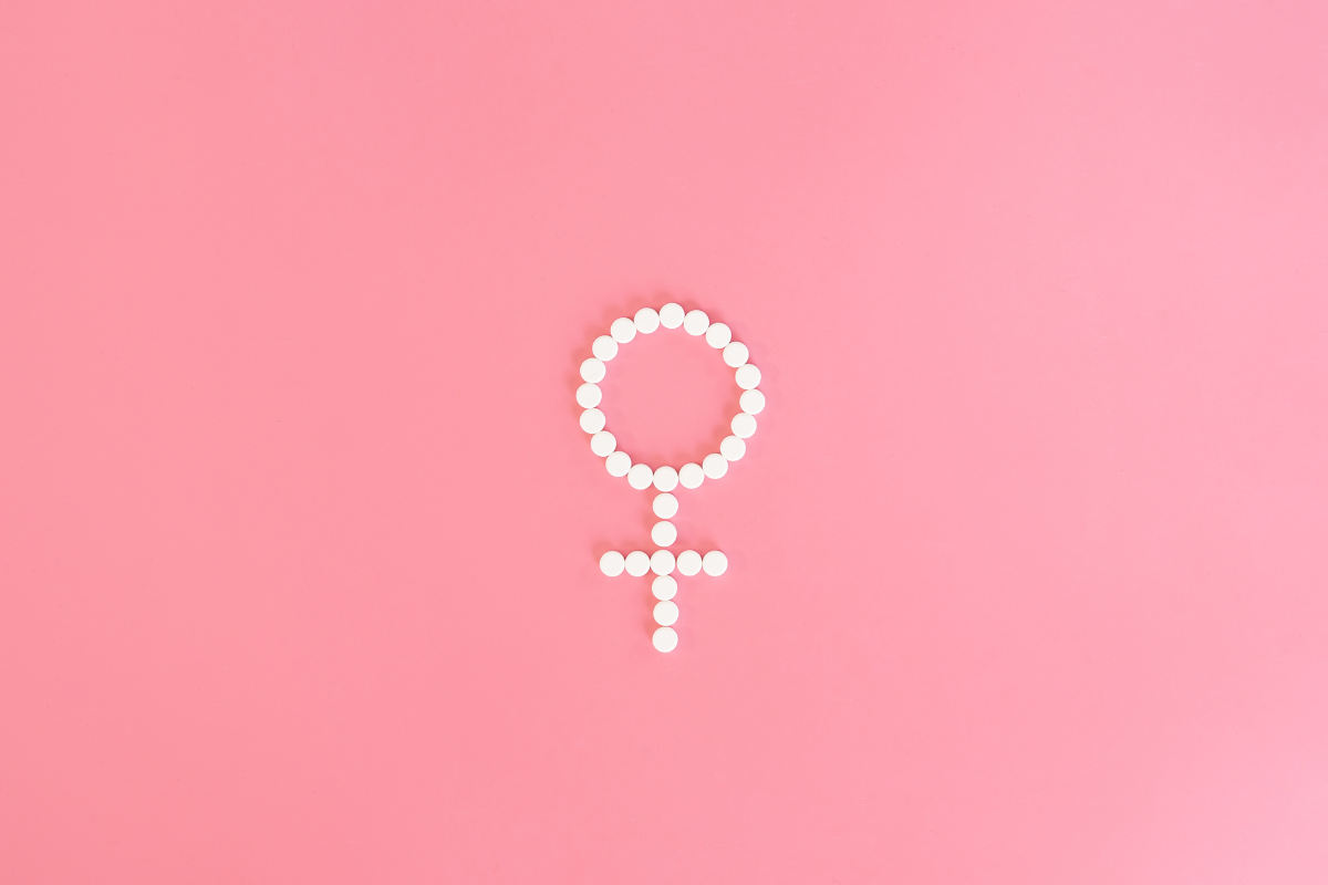 Un symbole féminin créé avec des pilules blanches sur fond rose, représentant la santé féminine et les sujets liés aux hormones et à la ménopause.