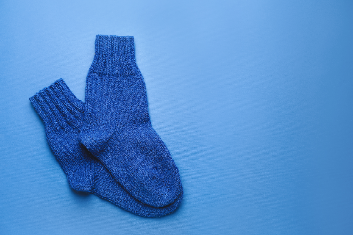 Une paire de chaussettes en laine d'un bleu profond reposant sur un fond bleu uni, évoquant la chaleur et le confort nécessaires pour les pieds pendant les mois d'hiver.