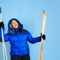 Une femme souriante en tenue d'hiver bleue tenant des skis et des bâtons de ski se prépare à profiter des sports d'hiver.