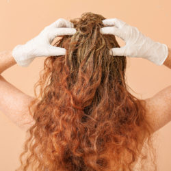 Mujer aplicándose colorante natural a base de henna en el pelo rizado