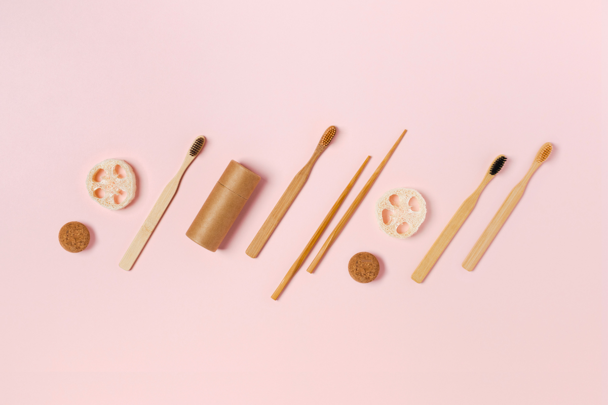 Zero-waste accessories for an eco-friendly bathroom: bamboo toothbrushes, natural loofahs and compostable cases on a pink background.