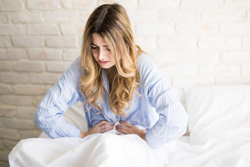 L'image représente une femme aux cheveux longs souffrant de colique hépatique. La jeune femme est pliée en deux et elle se tient le ventre avec les deux mains comme pour apaiser sa douleur;