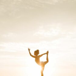 L'image représente une personne en train de faire du Yoga à la plage, durant un coucher de soleil. Nat & Form