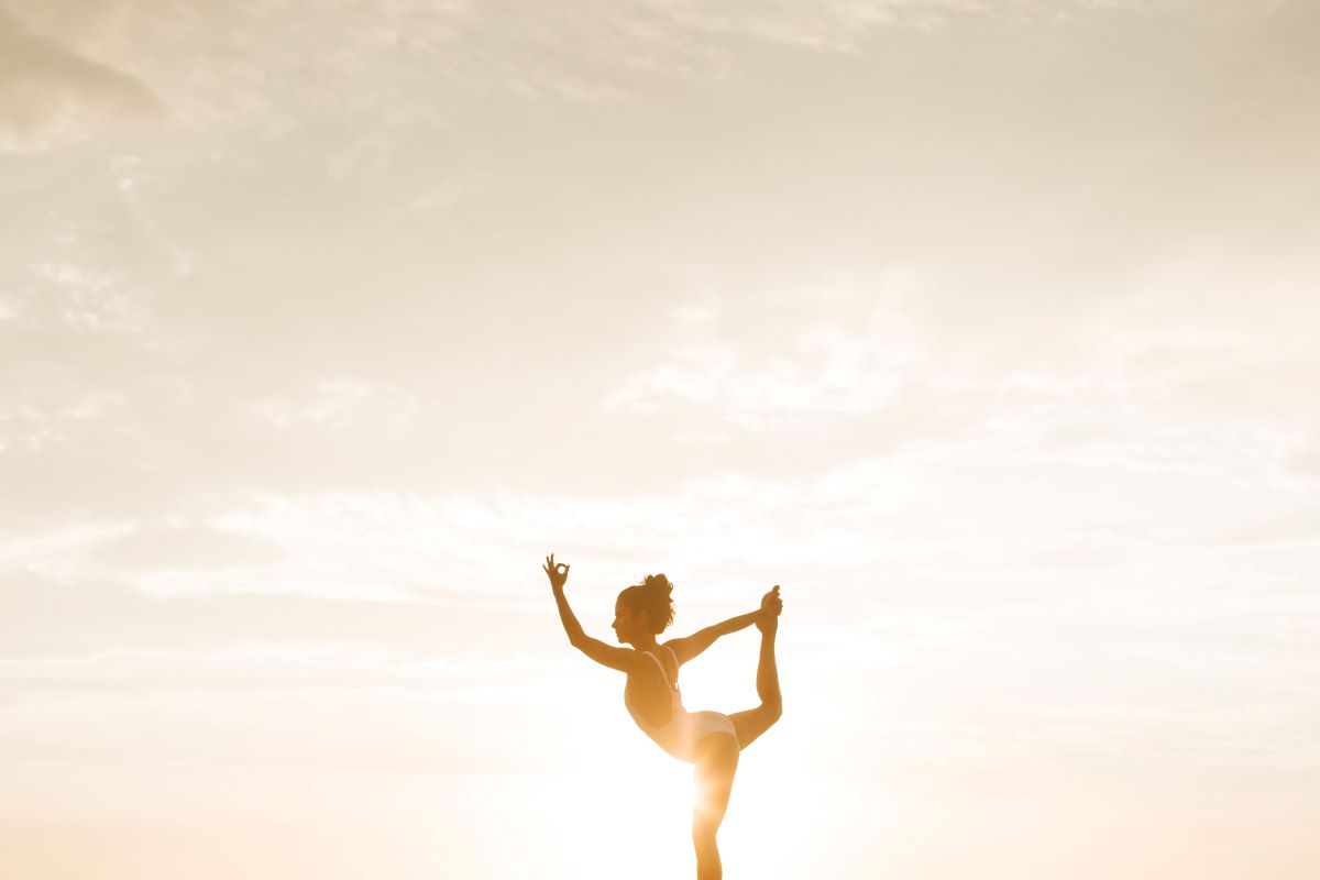 L'image représente une personne en train de faire du Yoga à la plage, durant un coucher de soleil. Nat & Form