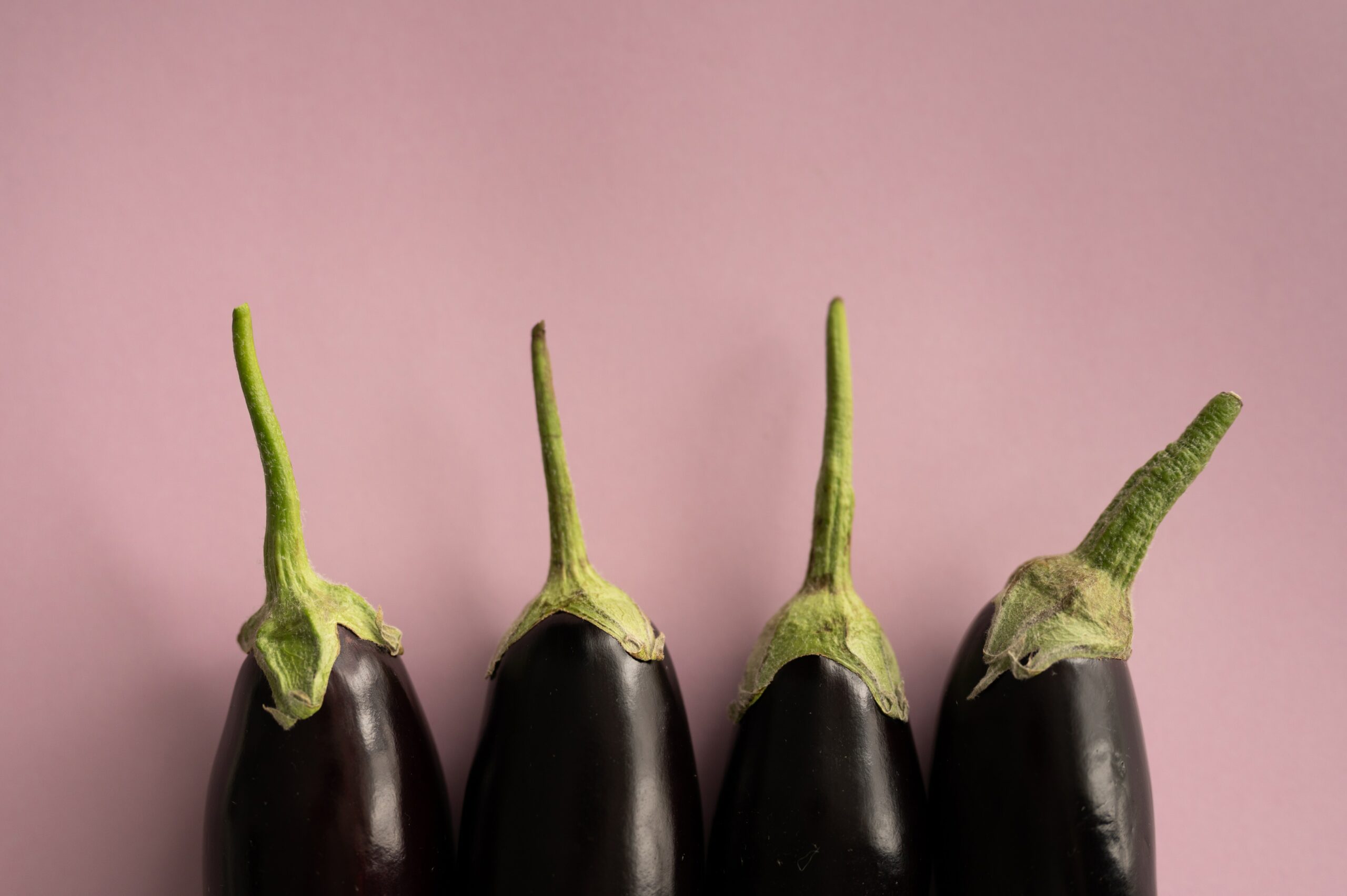 L'image représente des aubergines alignées sur un fond rose. Whole 30