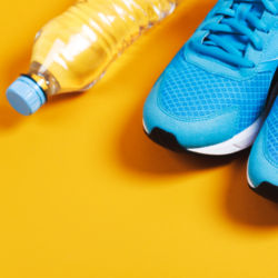 L'image représente un sol jaune sur lequel sont posés une paire de baskets et une bouteille d'eau. Petits conseils pour une reprise du sport en douceur