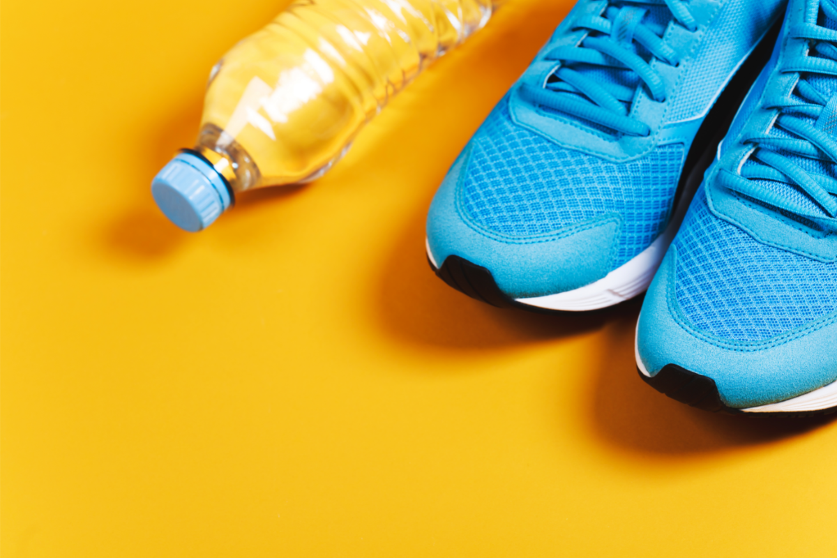 L'image représente un sol jaune sur lequel sont posés une paire de baskets et une bouteille d'eau. Petits conseils pour une reprise du sport en douceur