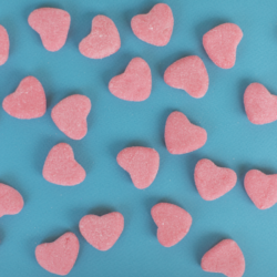 L'image représente des gummies en forme de cœurs roses sur un fond bleu vert. Du nouveau chez herbalgem heart shaped gummies