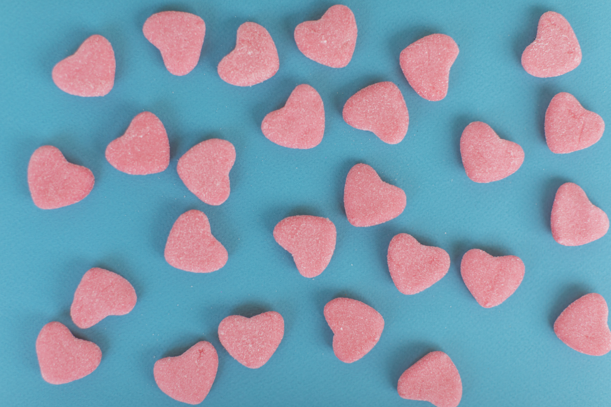 L'image représente des gummies en forme de cœurs roses sur un fond bleu vert. Du nouveau chez herbalgem heart shaped gummies