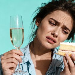 Femme fatiguée et dégoûtée au réveillon tenant un verre de champagne et une part de gâteau, illustration pour article sur les solutions naturelles pour survivre aux fêtes