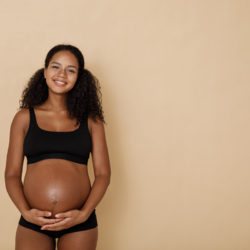 L'image représente une femme enceinte très souriante, qui se tient le ventre. les signes de la grossesse