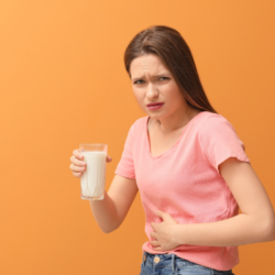 Comment choisir les granules d’homéopathie en cas d’indigestion ? L'image représente une jeune femme tenant un verre de lait, elle se touche le ventre en faisant la grimace pour montrer qu'elle a probablement du mal à digérer.