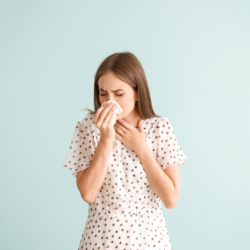 Une femme en blouse à pois tient un mouchoir contre son nez, apparemment en train d'éternuer ou de se moucher, illustrant les symptômes typiques d'une allergie comme le rhume des foins.