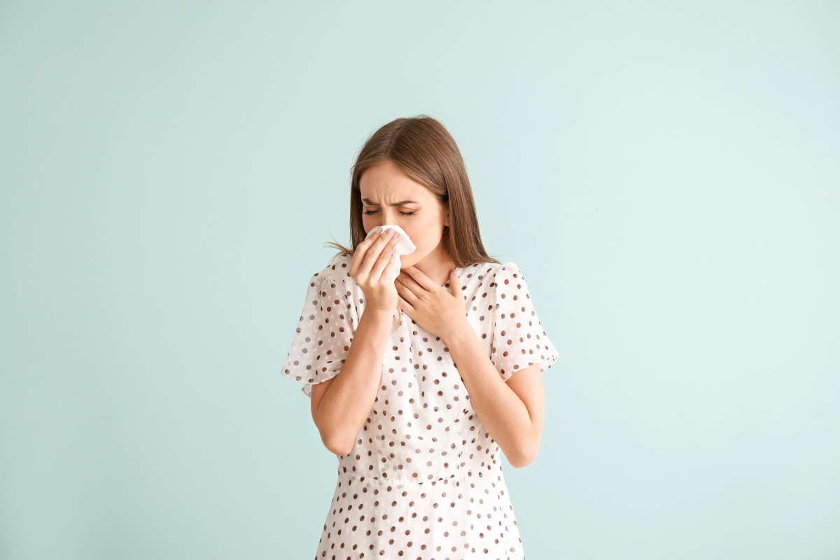 Une femme en blouse à pois tient un mouchoir contre son nez, apparemment en train d'éternuer ou de se moucher, illustrant les symptômes typiques d'une allergie comme le rhume des foins.