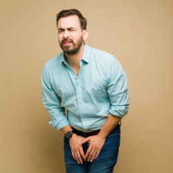 Homme tenant son bas-ventre avec une expression de douleur, indiquant une possible urgence urinaire ou inconfort.