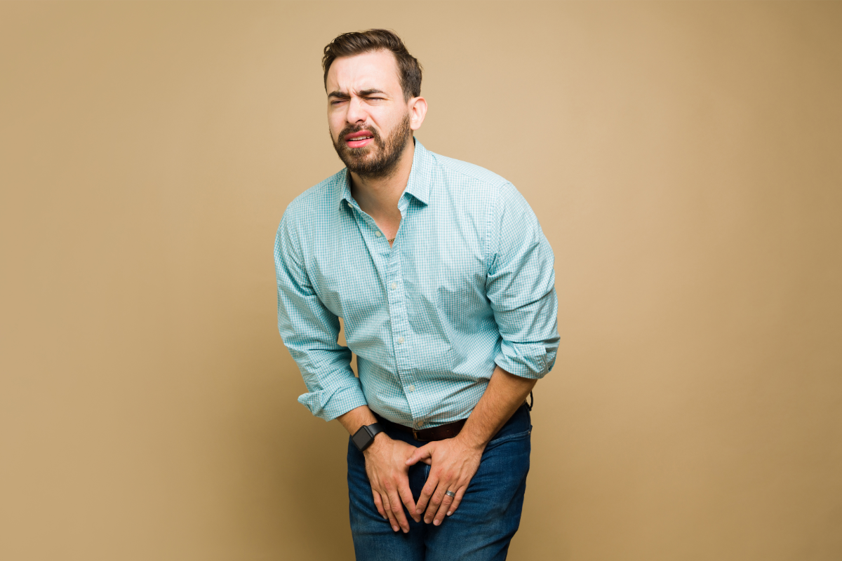 Homme tenant son bas-ventre avec une expression de douleur, indiquant une possible urgence urinaire ou inconfort.