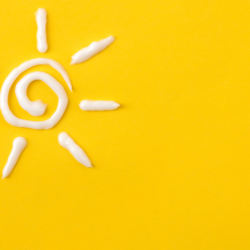 L'image représente un soleil dessiné avec de la crème solaire, sur un fond jaune pour illustrer l'article sur la protection solaire pour les cheveux cheveux