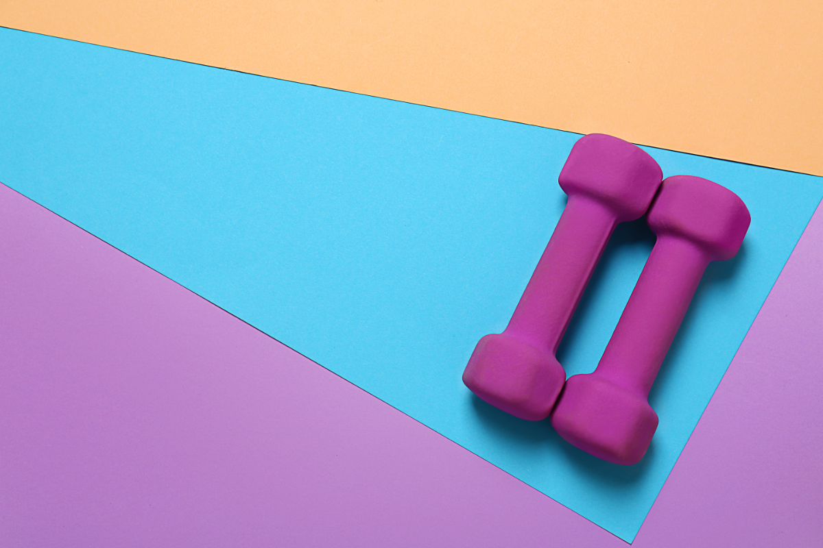 des haltères roses posées sur un tapis coloré pour illustrer le fait de faire du renforcement musculaire pour booster son métabolisme