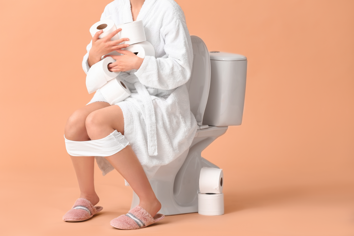 femme en peignoir sur les toilettes avec plusieurs rouleaux de papier toilette