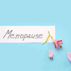 Ménopause écrit sur une carte blanche avec une fleur rose fanée sur un fond bleu clair. douleurs musculosquelettiques