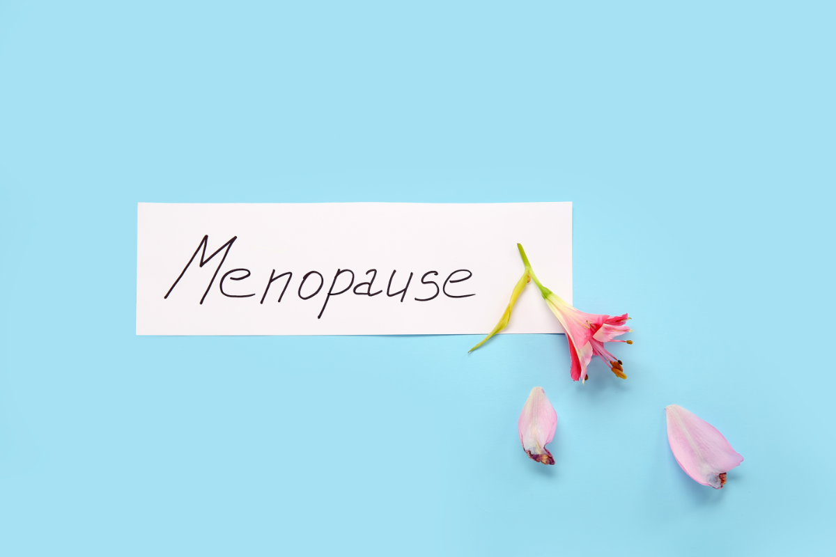 Ménopause écrit sur une carte blanche avec une fleur rose fanée sur un fond bleu clair. douleurs musculosquelettiques
