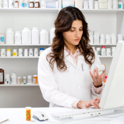 Une pharmacienne examine un médicament tout en travaillant sur un ordinateur dans une pharmacie. Cette image illustre le rôle crucial du pharmacien dans l'accompagnement des patients en surpoids ou obèses, notamment par des conseils nutritionnels et la recommandation de compléments alimentaires pour améliorer la santé intestinale et gérer le poids.