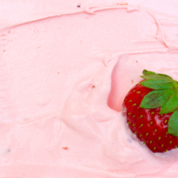 Une fraise fraîche posée sur une glace rose, illustrant l'utilisation courante des émulsifiants alimentaires dans les produits transformés comme les desserts glacés. Les émulsifiants sont utilisés pour stabiliser et améliorer la texture de ces produits, mais leur impact sur la santé suscite des préoccupations croissantes.