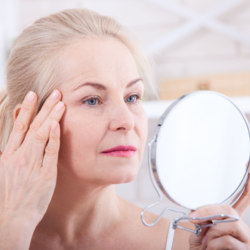 Une femme mature examine sa peau devant un miroir, illustrant les effets positifs de l’huile de Calophylle sur la stimulation de la production de collagène, contribuant à une peau plus ferme et plus lisse.