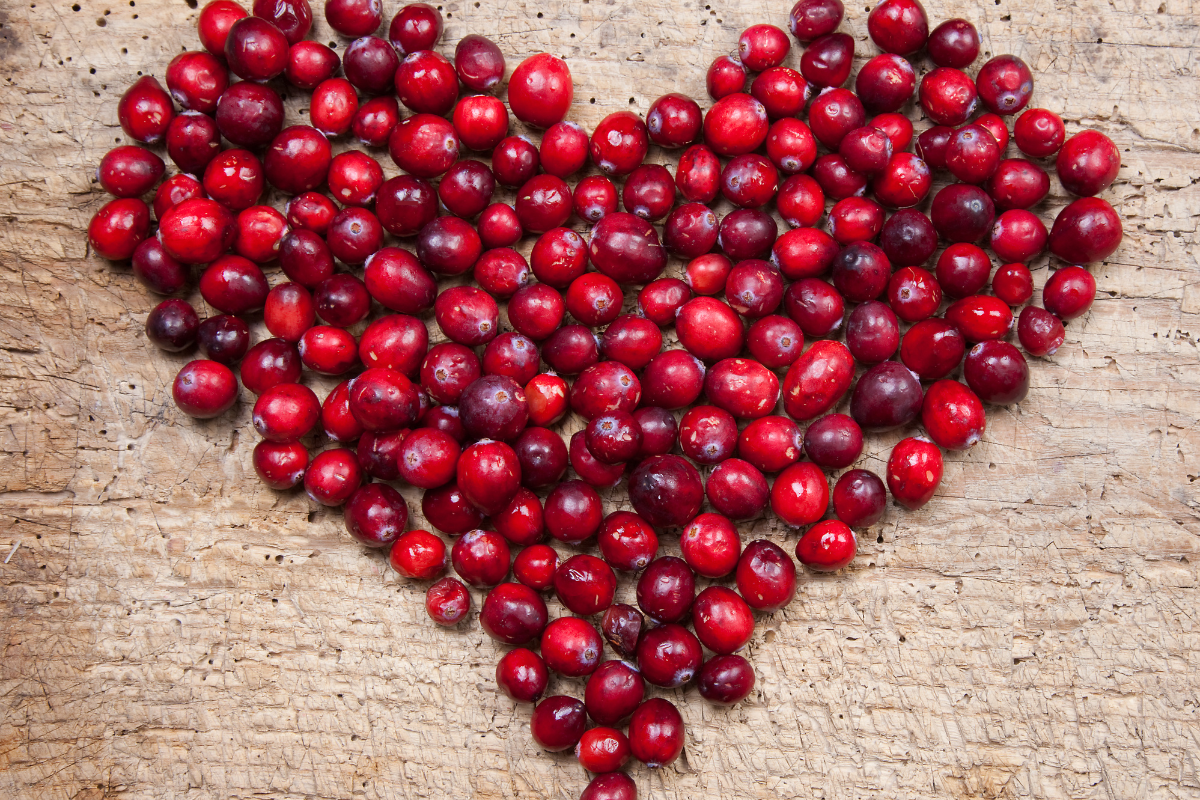 Fresh cranberries arranged in a heart shape on a wooden surface, illustrating the health benefits and anti-cancer potential of this superfood.